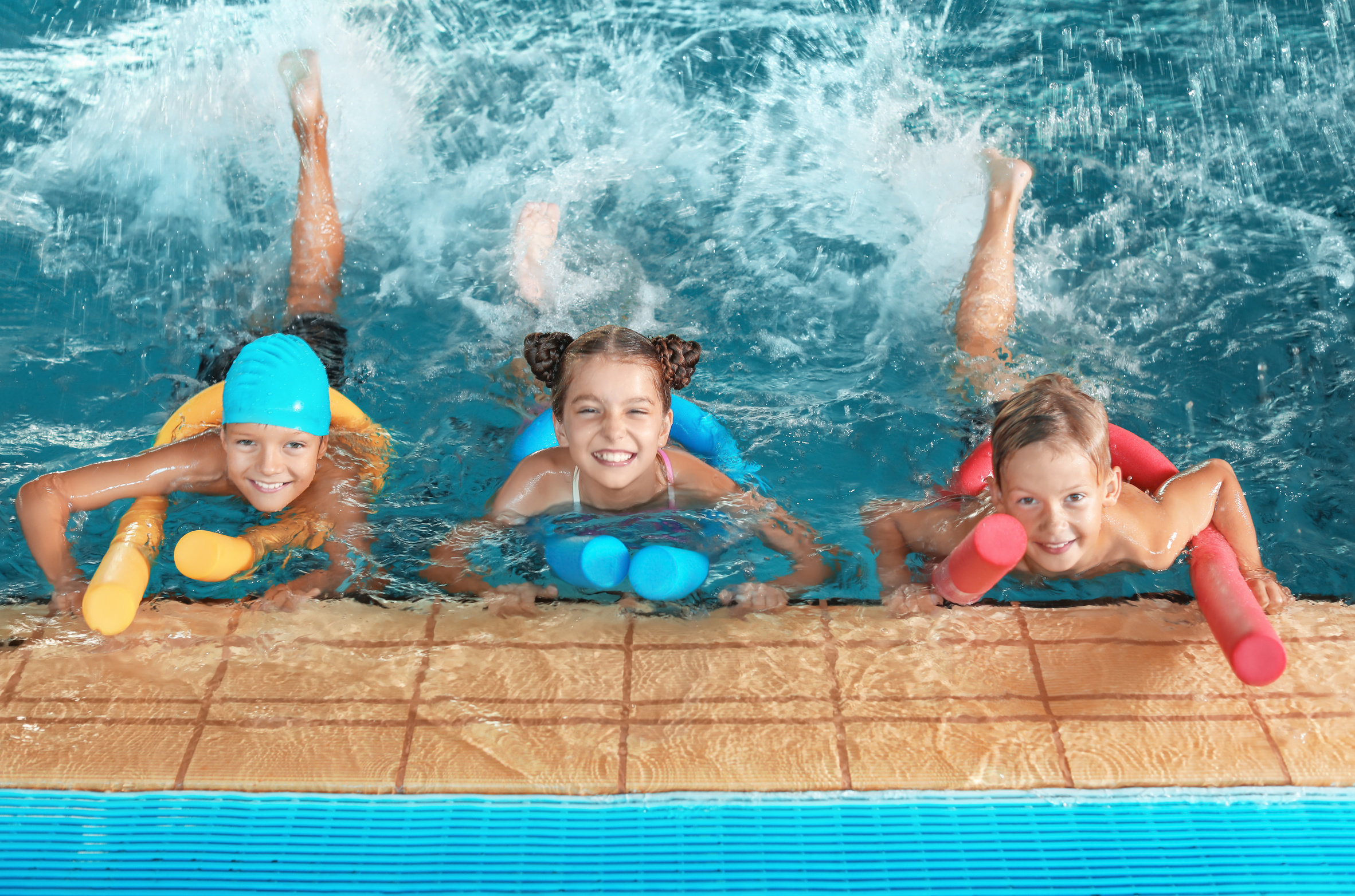 Little kids with swimming noodles in indoor pool